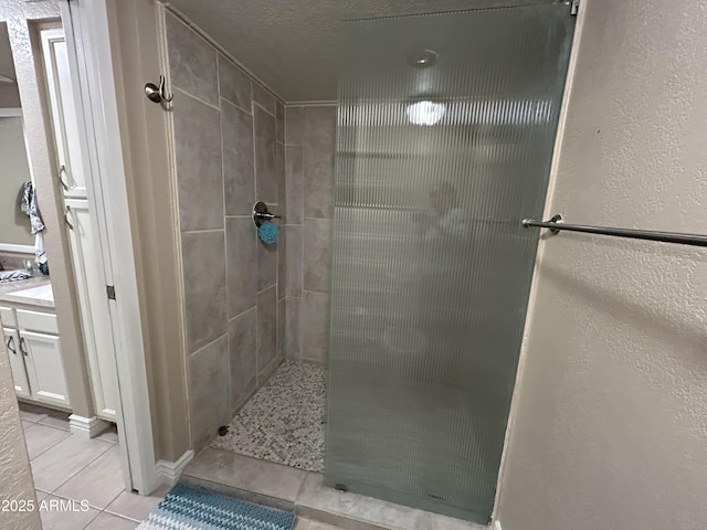 full bathroom with tile patterned flooring, a tile shower, and a textured wall