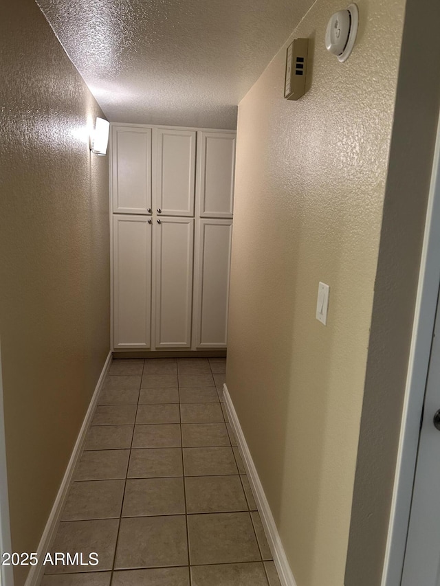 hall featuring baseboards, a textured ceiling, and light tile patterned floors