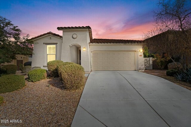 mediterranean / spanish home featuring a garage, a tiled roof, concrete driveway, and stucco siding