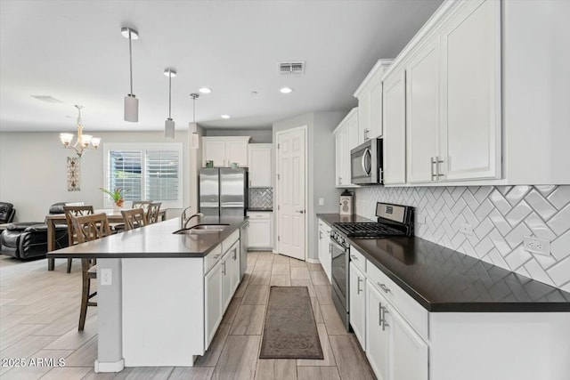 kitchen with a kitchen island with sink, stainless steel appliances, visible vents, white cabinetry, and dark countertops