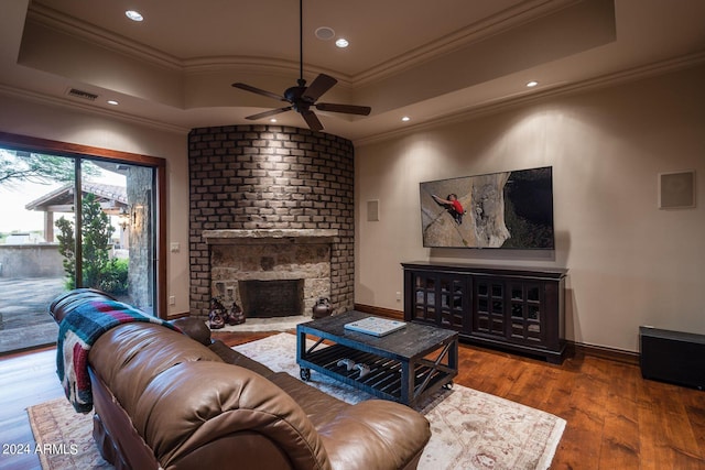 living room with hardwood / wood-style floors, a tray ceiling, ceiling fan, a fireplace, and crown molding