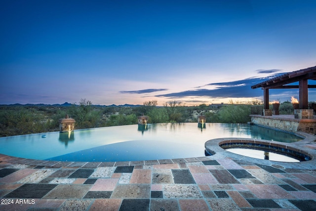 pool at dusk featuring a patio and an in ground hot tub