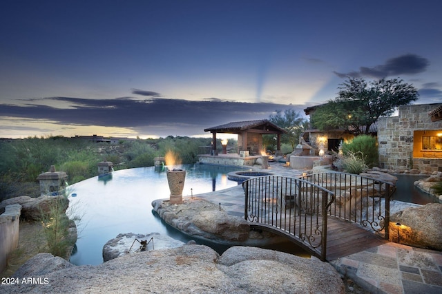 pool at dusk with an outdoor fireplace, a patio area, and a gazebo