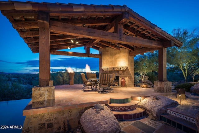 patio terrace at dusk featuring a gazebo and an outdoor stone fireplace