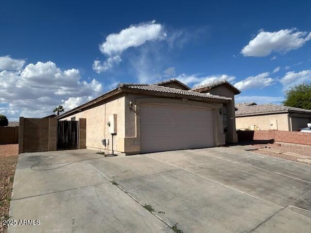 7664 W Vermont Ave, Glendale, AZ 85303 - view of side of home with concrete driveway, stucco siding, a tile roof, an attached garage, and a gate