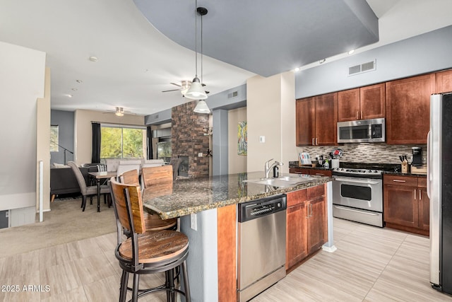 kitchen with sink, tasteful backsplash, a center island with sink, dark stone countertops, and stainless steel appliances