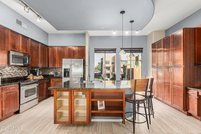 kitchen with stainless steel appliances, sink, hanging light fixtures, and a center island with sink