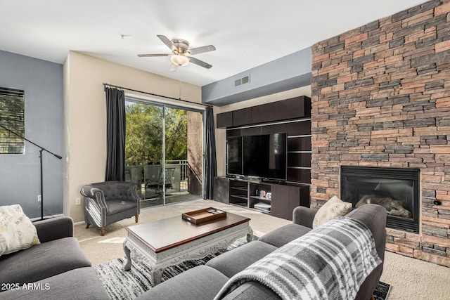 living room featuring light carpet, a stone fireplace, and ceiling fan