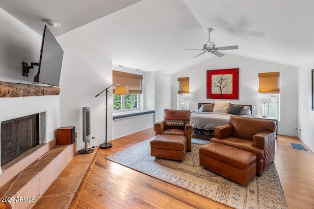 bedroom with vaulted ceiling, visible vents, a fireplace with raised hearth, and wood finished floors