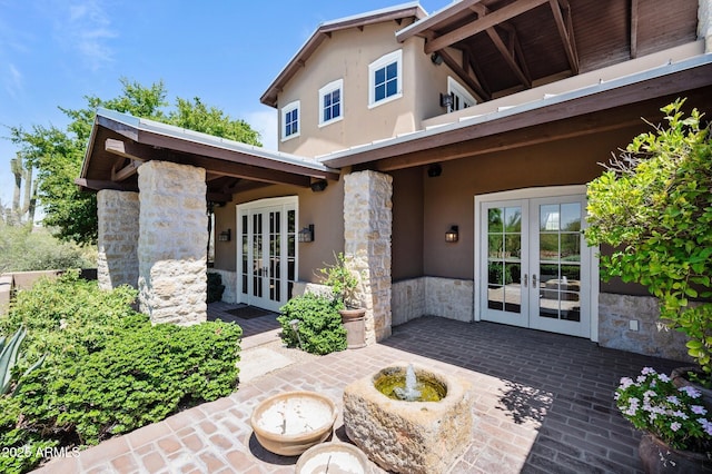 exterior space featuring stone siding, a patio area, stucco siding, and french doors