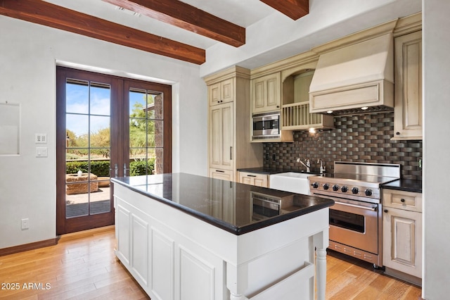 kitchen with cream cabinetry, dark countertops, custom range hood, backsplash, and appliances with stainless steel finishes