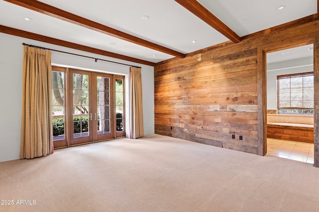 carpeted spare room with wood walls, beam ceiling, and french doors