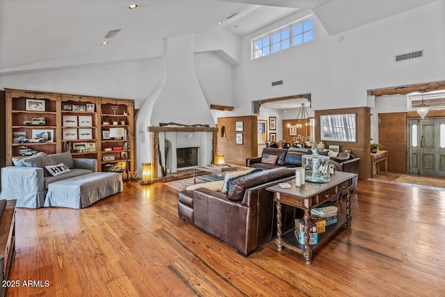 living area with high vaulted ceiling, a fireplace, wood finished floors, and visible vents