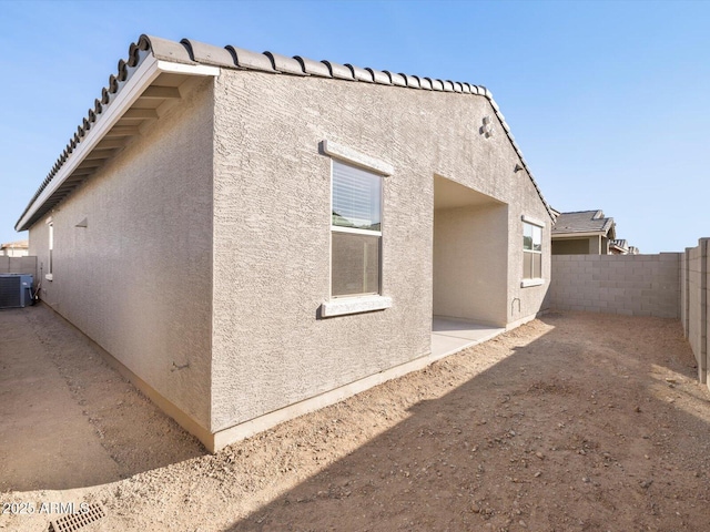 view of side of home featuring a fenced backyard, a patio, central AC, and stucco siding