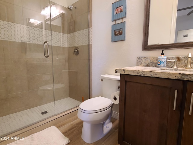 bathroom with vanity, hardwood / wood-style flooring, ceiling fan, toilet, and a shower with shower door