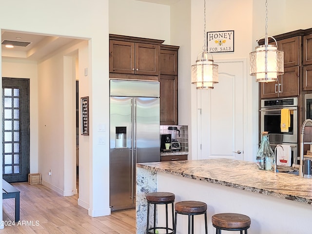 kitchen with light stone countertops, light wood-type flooring, a breakfast bar, stainless steel appliances, and decorative light fixtures