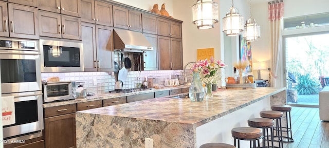 kitchen with hardwood / wood-style flooring, light stone countertops, tasteful backsplash, a kitchen bar, and stainless steel appliances