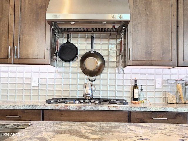 kitchen with tasteful backsplash, light stone counters, exhaust hood, and stainless steel gas cooktop