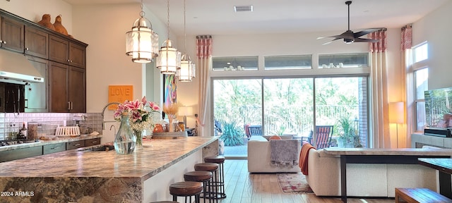 kitchen featuring backsplash, dark brown cabinetry, stainless steel gas cooktop, pendant lighting, and light hardwood / wood-style flooring