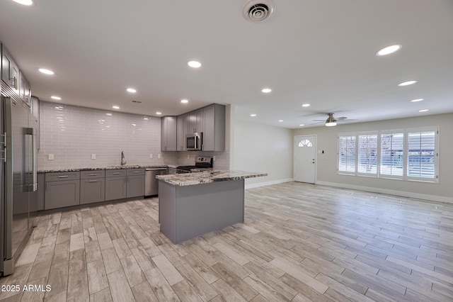 kitchen with gray cabinets, appliances with stainless steel finishes, light stone counters, decorative backsplash, and kitchen peninsula