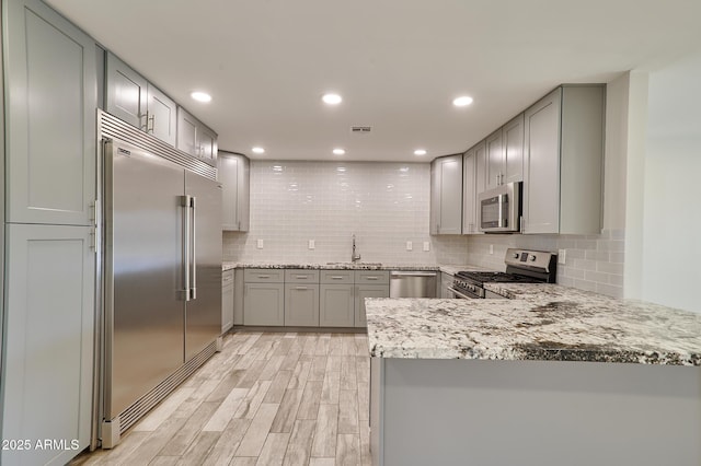 kitchen with sink, decorative backsplash, kitchen peninsula, stainless steel appliances, and light wood-type flooring