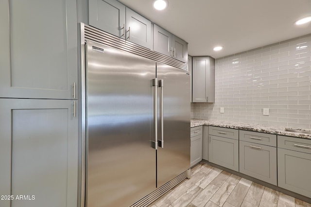 kitchen with gray cabinetry, backsplash, light hardwood / wood-style floors, and stainless steel built in refrigerator