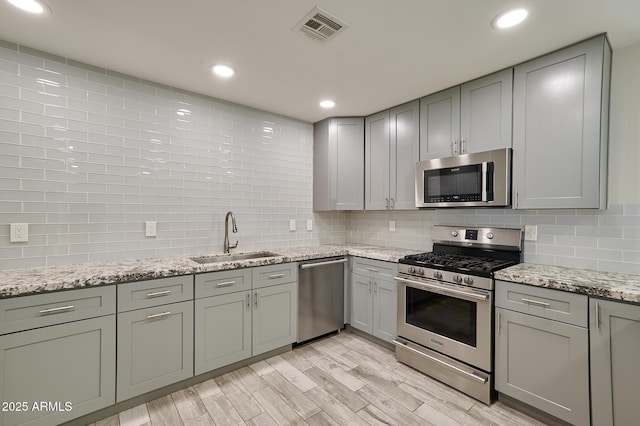 kitchen featuring sink, light stone counters, light wood-type flooring, stainless steel appliances, and decorative backsplash