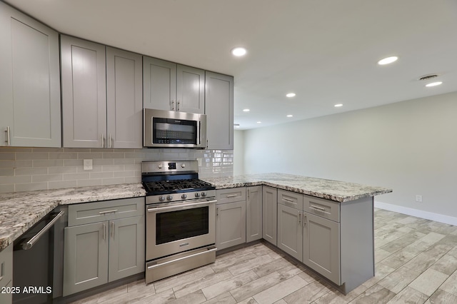 kitchen featuring tasteful backsplash, stainless steel appliances, kitchen peninsula, and light stone countertops