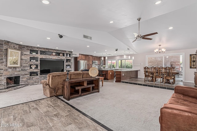 living room with visible vents, lofted ceiling, a stone fireplace, recessed lighting, and ceiling fan with notable chandelier