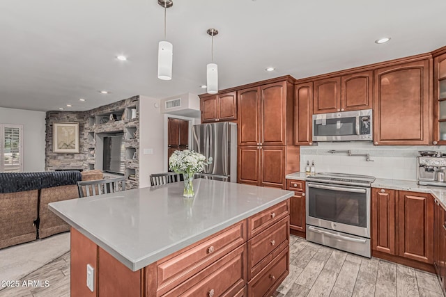kitchen with appliances with stainless steel finishes, light countertops, backsplash, visible vents, and a kitchen island