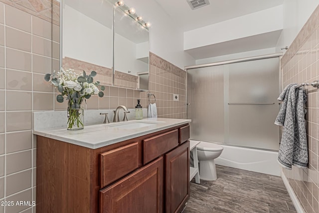 bathroom featuring visible vents, vanity, toilet, tile walls, and bath / shower combo with glass door