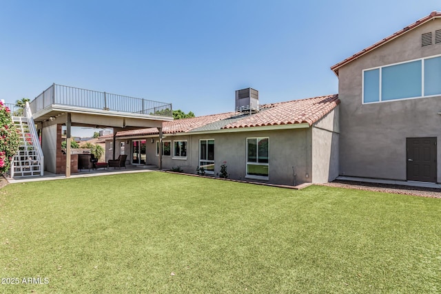 back of property featuring stucco siding, a chimney, stairs, a tiled roof, and a yard