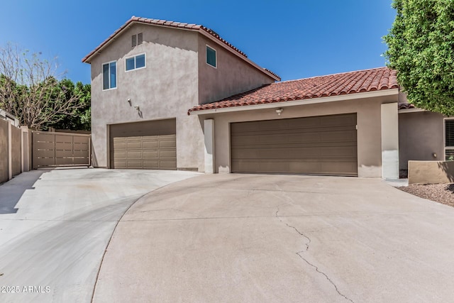 mediterranean / spanish-style home featuring a tiled roof, stucco siding, driveway, and fence