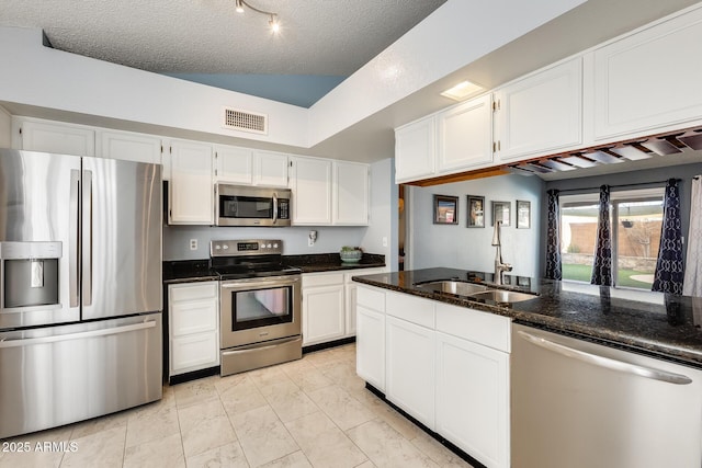 kitchen featuring sink, dark stone countertops, white cabinets, stainless steel appliances, and a textured ceiling