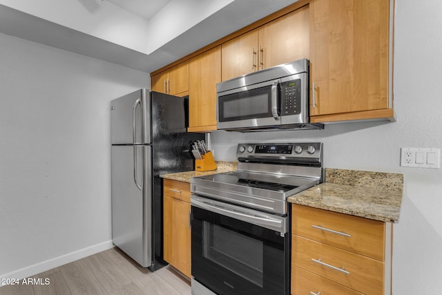 kitchen featuring light stone countertops, appliances with stainless steel finishes, and light wood-type flooring