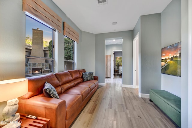 living area with a fireplace, baseboards, visible vents, and light wood-style floors