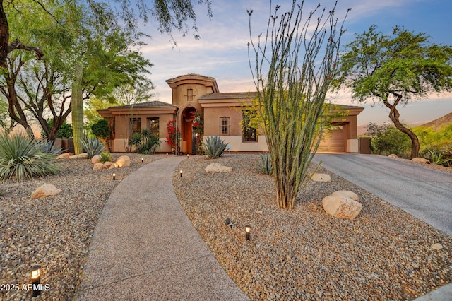 mediterranean / spanish-style home with an attached garage, aphalt driveway, and stucco siding