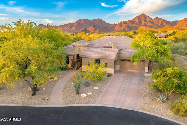view of front facade with stucco siding, a tiled roof, an attached garage, a mountain view, and driveway