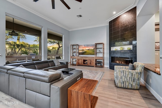living area with crown molding, ceiling fan, a fireplace, light wood-type flooring, and visible vents