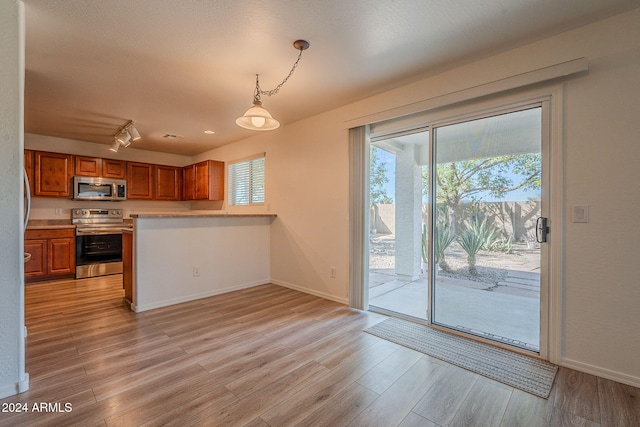 kitchen with light hardwood / wood-style floors, kitchen peninsula, appliances with stainless steel finishes, rail lighting, and decorative light fixtures