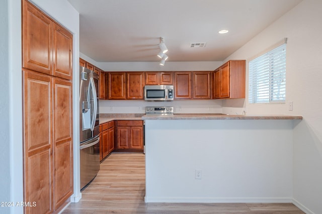 kitchen with kitchen peninsula, rail lighting, light wood-type flooring, and appliances with stainless steel finishes