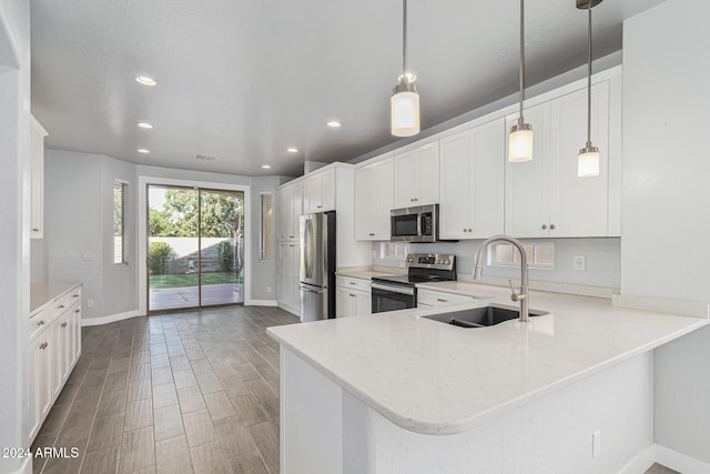 kitchen featuring white cabinetry, sink, kitchen peninsula, decorative light fixtures, and appliances with stainless steel finishes