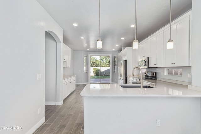 kitchen featuring kitchen peninsula, stainless steel appliances, decorative light fixtures, hardwood / wood-style flooring, and white cabinetry