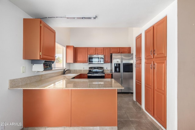 kitchen with kitchen peninsula, stainless steel appliances, tile patterned flooring, light stone counters, and sink