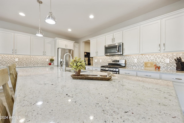 kitchen with light stone countertops, pendant lighting, white cabinets, and stainless steel appliances