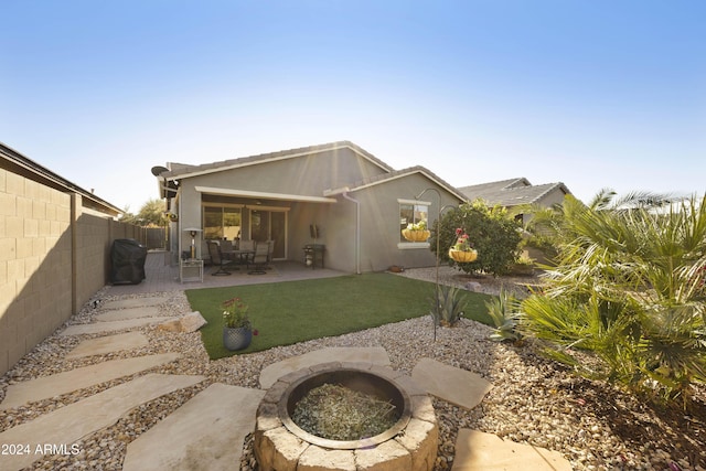 back of house featuring a lawn, a patio, and a fire pit