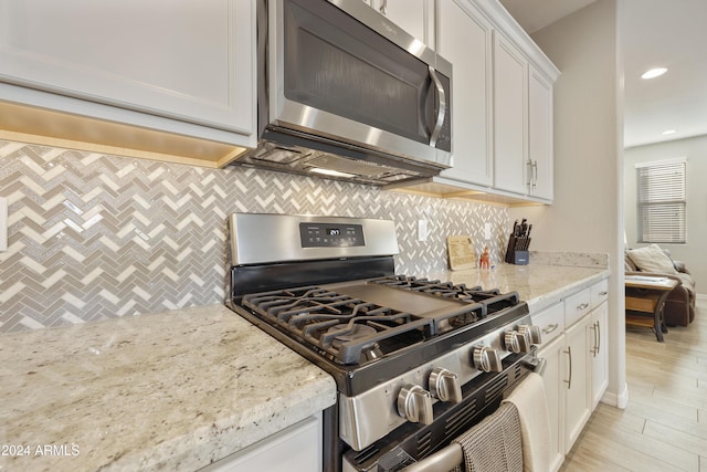 kitchen featuring appliances with stainless steel finishes, backsplash, light stone counters, light hardwood / wood-style floors, and white cabinetry