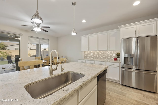 kitchen featuring white cabinetry, sink, light stone counters, decorative light fixtures, and appliances with stainless steel finishes