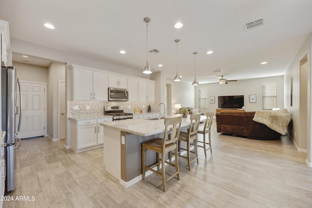 kitchen with white cabinetry, light stone countertops, an island with sink, decorative light fixtures, and appliances with stainless steel finishes