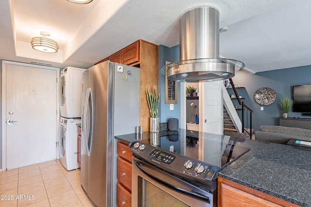 kitchen featuring light tile patterned flooring, a raised ceiling, island exhaust hood, stacked washer / drying machine, and stainless steel appliances